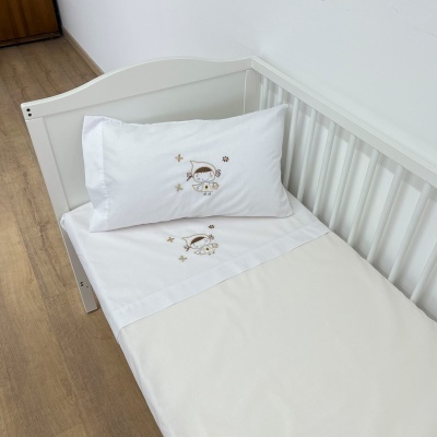 Cama de bebé com roupa de cama branca e bordados de menino e estrelas castanhas