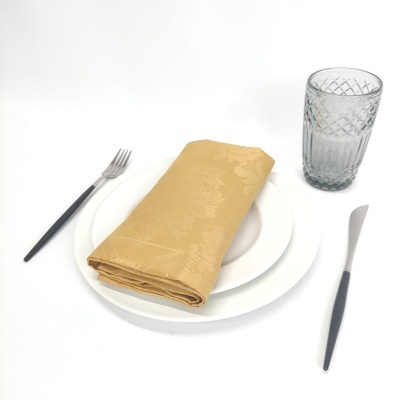 Conjunto de jantar com pratos brancos, guardanapo amarelo, talheres pretos e copo cinzento