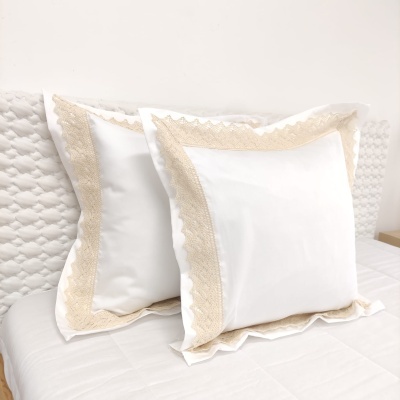 Duas almofadas brancas com bordado de renda bege numa cama branca.