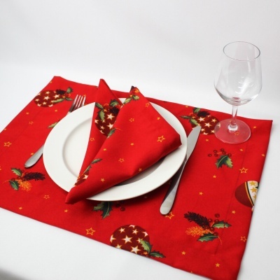 Guardanapo e pega de panela vermelhos com padrão de Natal, prato branco, talheres e taça de vidro
