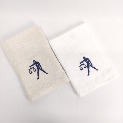 Dois toalhetes, bege e branco, com bordado azul de figura segurando uma balança