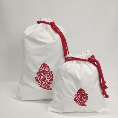 Dois sacos de pano brancos com cordão vermelho e padrão bordado vermelho.
