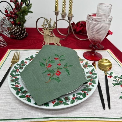 Mesa decorada para Natal com pratos e guardanapo verde bordado, talheres pretos e dourados, copos rosa, castiçal dourado e enfeites natalícios