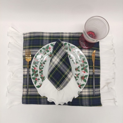 Conjunto de mesa com prato decorado, guardanapo xadrez, faca e garfo dourados e copo transparente com base vermelha.