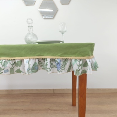 Toalha de mesa verde com franja floral numa mesa de madeira com um prato, decanter e taça.