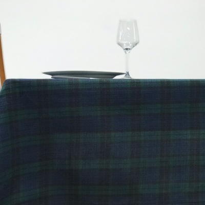 Toalha de mesa xadrez azul e verde escuro com prato cinza e copo de vidro sobre mesa