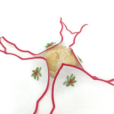 Guardanapo branco com bordas vermelhas e bordados verdes e vermelhos envolvendo pão.