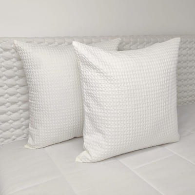 Três almofadas brancas texturizadas sobre colchão branco com cabeceira acolchoada.