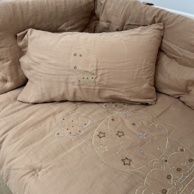 Capa de almofada e lençol castanho claro com bordados de estrelas, balão, ursinhos e nuvens.