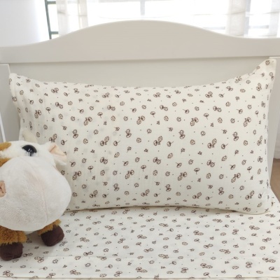 Travesseiro com fronha branca com padrão de flores castanhas numa cama branca junto a pelúcia