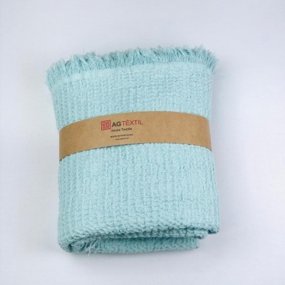 Manta azul claro com textura quadriculada e franjas, com faixa de papel AG TEXTIL