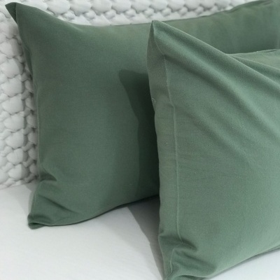 Duas almofadas verdes sobre cama branca com cabeceira texturada