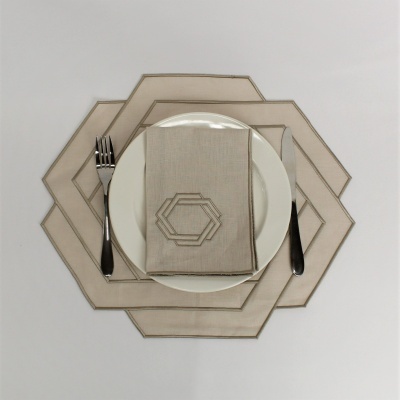 Conjunto de jantar com prato branco e guardanapo cinzento com bordado geometricamente colocado em sousplats cinzentos.