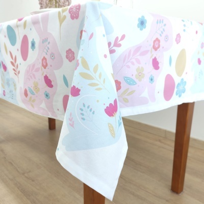 Toalha de mesa branca com coelhos e flores coloridas em mesa de madeira