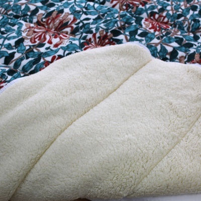 Manta creme felpuda sobre tecido com estampado floral verde e vermelho