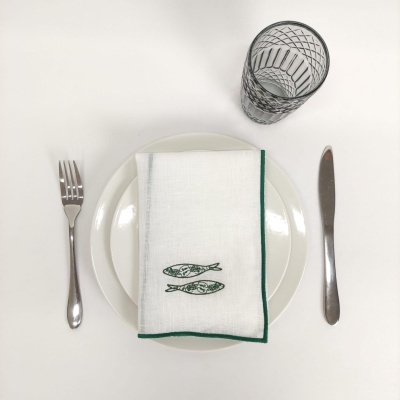 Conjunto de talheres, prato branco, toalha com bordado de peixes e copo de vidro