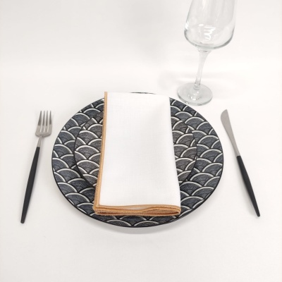 Conjunto de jantar com prato decorado em tons azuis, guardanapo branco, talheres com cabo preto e copo transparente.