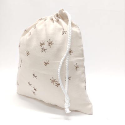 Saco de pano branco com padrão de pequenos insetos castanhos e cordão de cierre branco.
