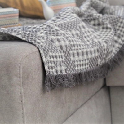 Cobertor cinzento com padrão branco sobre sofá cinzento claro