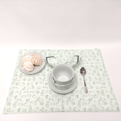 Jogo americano com padrão de coelhos, chávena, pires, colher e prato com bolos