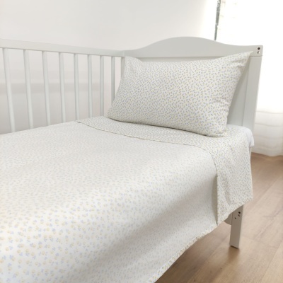 Lençóis de cama de bebé em algodão com padrão floral amarelo e azul em cama branca de madeira.