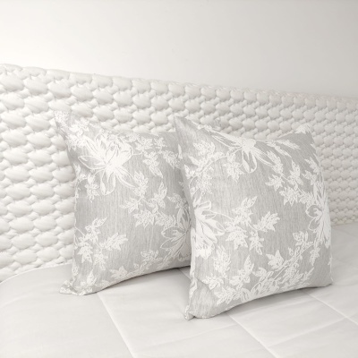 Duas almofadas cinzentas com padrão floral branco sobre cama branca com cabeceira trançada branca