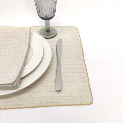 Conjunto de mesa com individual bege, guardanapo listrado, pratos brancos, faca e copo cinza com padrão