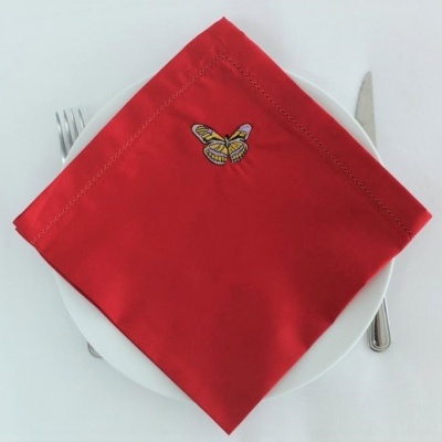 Guardanapo vermelho com bordado de borboleta sobre prato branco com talheres