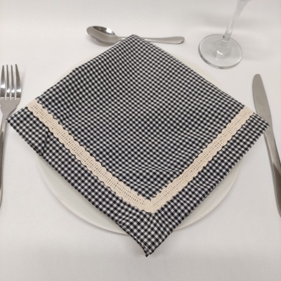 Guardanapo xadrez preto e branco com borda rendada sobre prato branco numa mesa posta