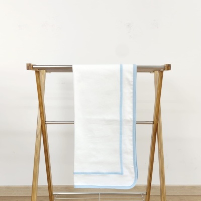 Toalha branca com borda azul pendurada em estendal de madeira