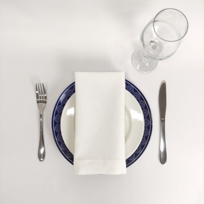 Mesa posta com prato, talheres, guardanapo branco e copo de vidro