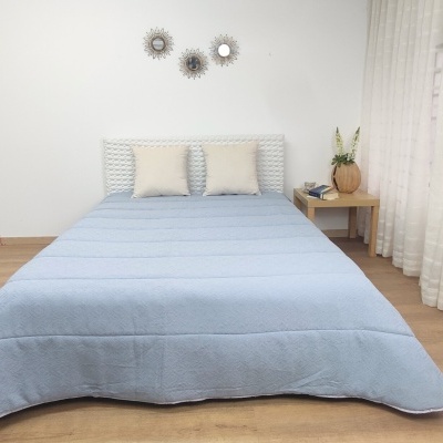 Cama com edredão azul claro e almofadas bege em quarto minimalista com mesa de cabeceira e decoração de parede
