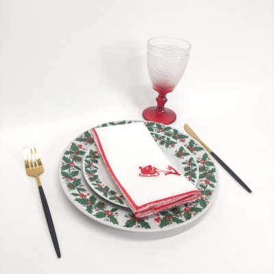 Conjunto de jantar com pratos natalícios, guardanapo branco bordado, copo com pé vermelho e talheres preto e dourado