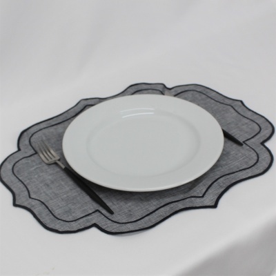 Prato branco redondo sobre individual cinzento com bordas pretas, com talheres de cabo preto numa superfície branca