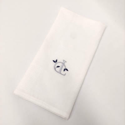 Guardanapo branco em tecido com bordado azul das letras JC.