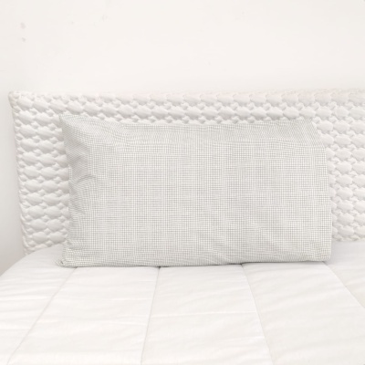 Almofada cinzenta quadriculada sobre cama branca acolchoada com cabeceira branca texturada