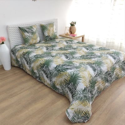 Cama com roupa de cama de padrão de folhas verdes e amarelas em fundo branco num quarto luminoso