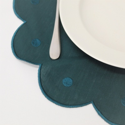 Individual de mesa verde escuro com padrão de círculos azuis e prato branco com colher