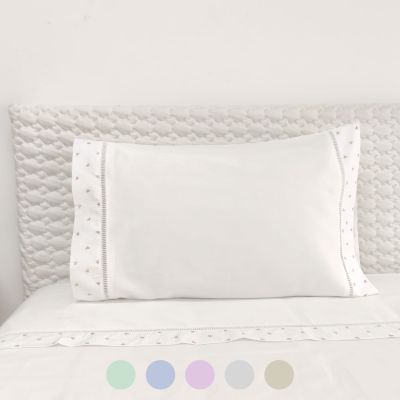 Almofada branca com bordado dourado em cama com cabeceira texturizada branca