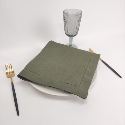 Talheres dourado e preto, prato branco com guardanapo verde e copo de vidro gravado