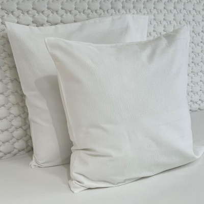 Duas almofadas brancas quadradas com texturas finas em fundo branco texturizado