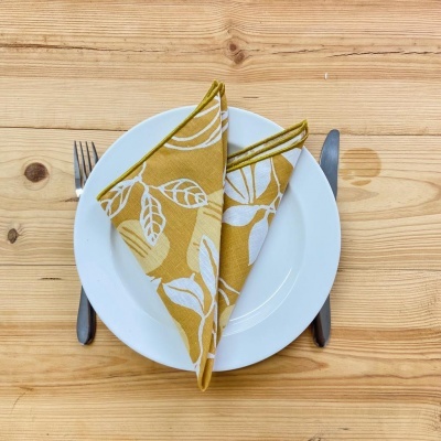 Prato branco com guardanapo amarelo estampado, talheres metálicos e mesa de madeira