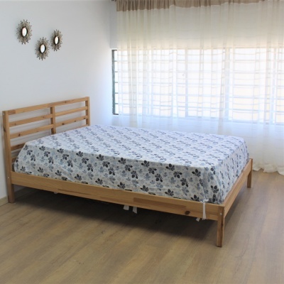 Cama de madeira clara com lençol branco e padrão floral num quarto com três espelhos redondos e cortinas brancas