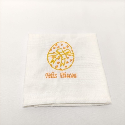 Guardanapo branco com bordado de ovo de Páscoa amarelo e laranja e texto Feliz Páscoa