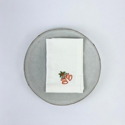 Guardanapo branco com bordado de sinos vermelhos e folhas verdes sobre prato cinza