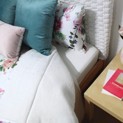 Cama com almofadas de várias cores e padrão floral ao lado de mesa com livro e vaso de flores