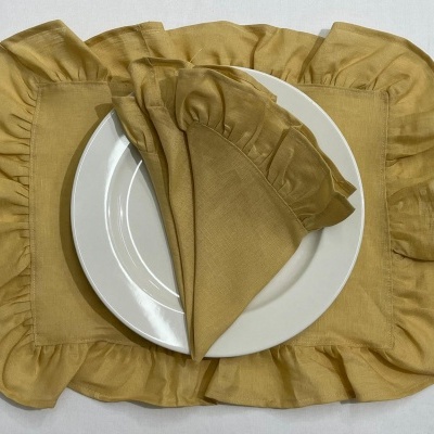 Conjunto de jogo de mesa amarelo com babados, prato branco sobre individual e guardanapo.