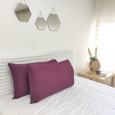 Cama com almofadas roxas, cabeceira branca, três espelhos hexagonais e mesa lateral com vaso