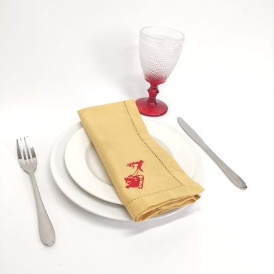 Conjunto de jantar com pratos brancos, talheres metálicos, copo de vidro com pé vermelho e guardanapo amarelo bordado.