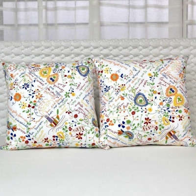 Par de almofadas decorativas com padrão floral colorido e texto em fundo branco em sofá branco